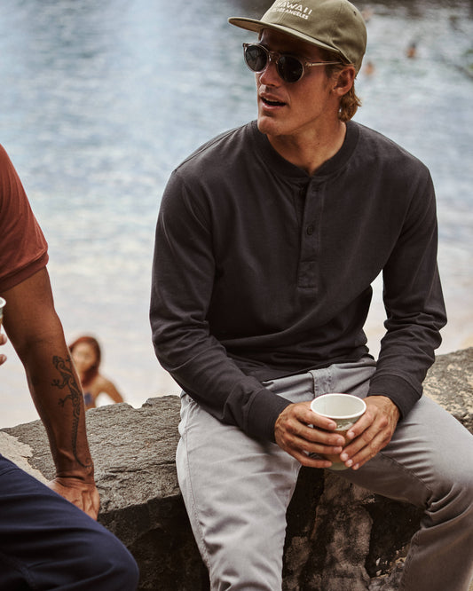 Man wearing black henley shirt sitting on a stone wall