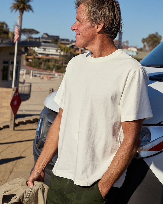 Man wearing white short-sleeved t-shirt leaning on a car