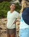A woman smiling and wearing a cream crewneck sweatshirt, standing on a beach