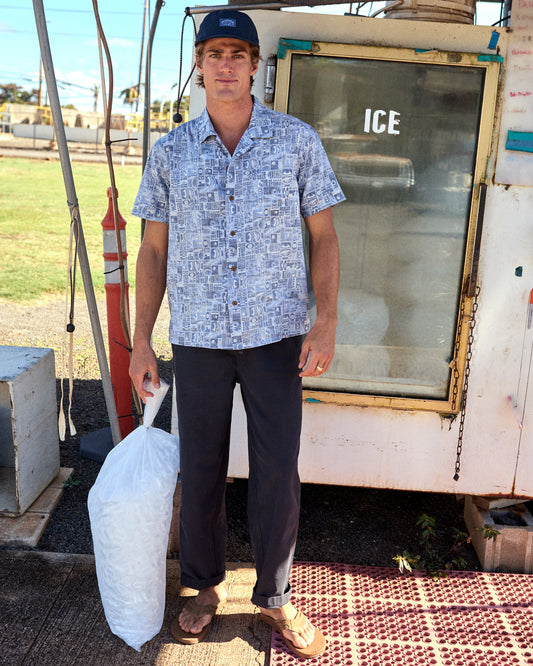 Man wearing a blue patterned button down holding a bag of ice