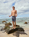 Man wearing blue boardshorts with a drawstring waistband at the beach.