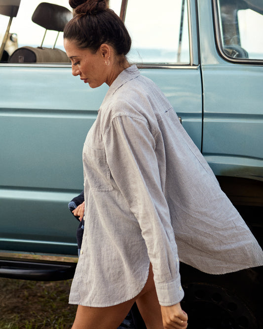woman in black and white pinstriped flowy button up with a  car in the background