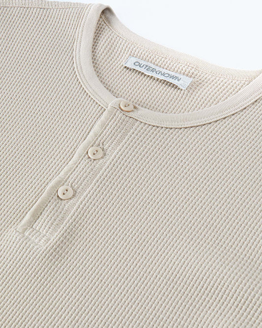 Close-up of a beige textured shirt with button details and a brand label on a white background