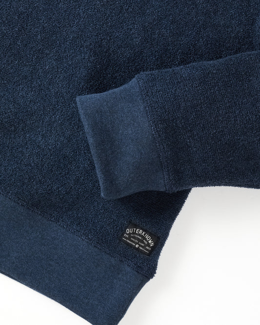 Closeup of navy blue crewneck sweatshirt made from terry toweling fabric, with a visible brand tag on the lower side.