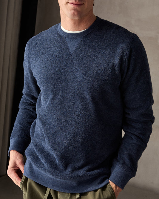 Man wearing a navy blue crewneck sweatshirt made from terry toweling fabric, with a visible brand tag on the lower side.