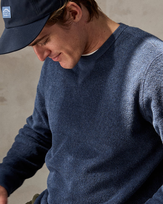 Man wearing a navy blue crewneck sweatshirt made from terry toweling fabric, with a visible brand tag on the lower side.