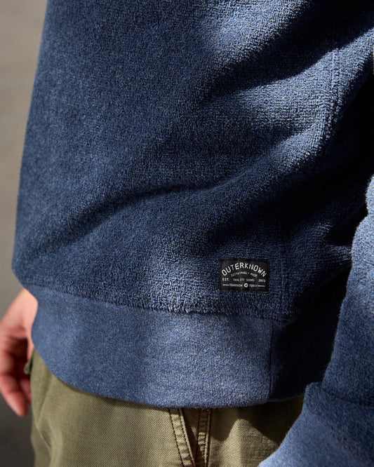 Closeup of navy blue crewneck sweatshirt made from terry toweling fabric, with a visible brand tag on the lower side.