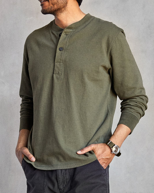 Man wearing a long-sleeved green henley shirt with a ribbed neckline and cuffs, featuring a minimal 2-button placket and flatlock seams.