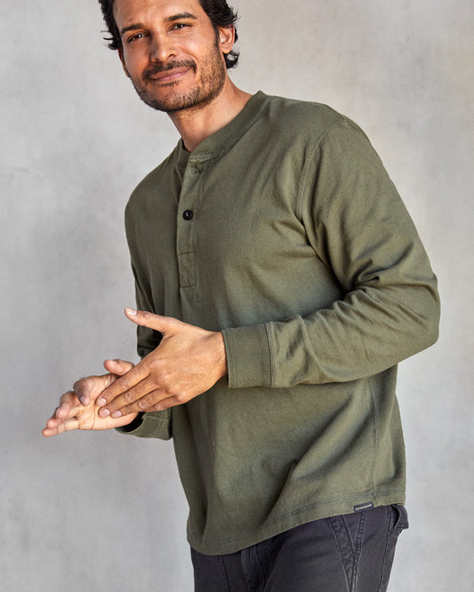 Man wearing a long-sleeved green henley shirt with a ribbed neckline and cuffs, featuring a minimal 2-button placket and flatlock seams.