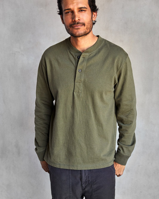 Man wearing a long-sleeved green henley shirt with a ribbed neckline and cuffs, featuring a minimal 2-button placket and flatlock seams.