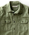 Closeup of a green, long-sleeved utilitarian shirt with a herringbone texture and chest pockets.