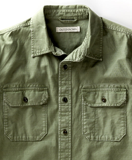 Closeup of a green, long-sleeved utilitarian shirt with a herringbone texture and chest pockets.