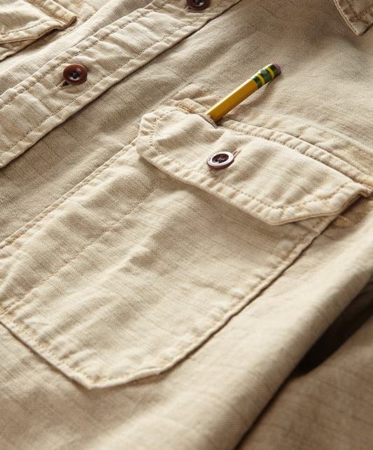 Closeup of a long-sleeved, button-up, beige utilitarian shirt with chest pockets.