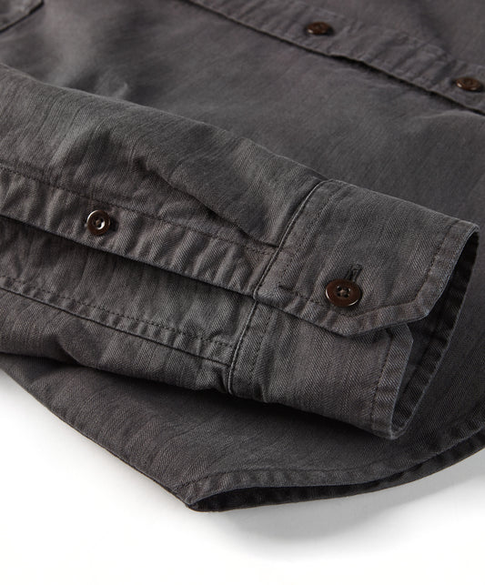 A long-sleeved black shirt with a herringbone texture, featuring a collar, button-up front, and two chest pockets.
