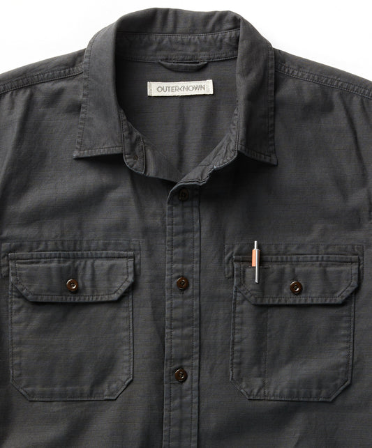 A long-sleeved black shirt with a herringbone texture, featuring a collar, button-up front, and two chest pockets.