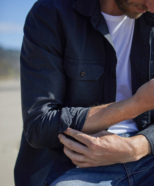 Man wearing a long-sleeved black shirt with a herringbone texture, featuring a collar, button-up front, and two chest pockets.