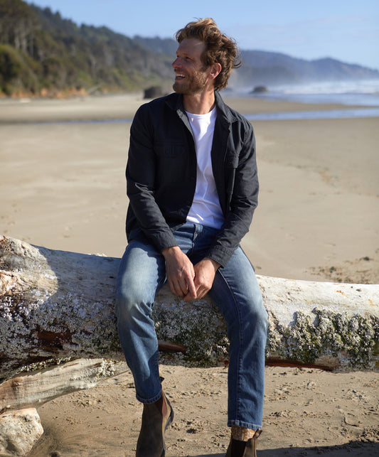 Man wearing a long-sleeved black shirt with a herringbone texture, featuring a collar, button-up front, and two chest pockets.
