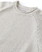 Close-up of a beige knit sweater with Outerknown branding on a white background