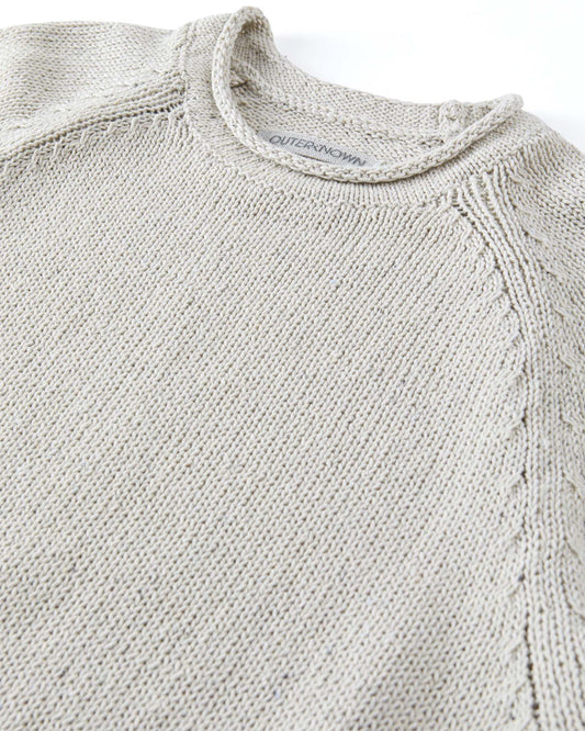 Close-up of a beige knit sweater with Outerknown branding on a white background