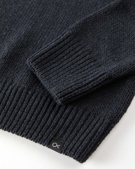 Close-up of a black sweater with a brand logo on a white background
