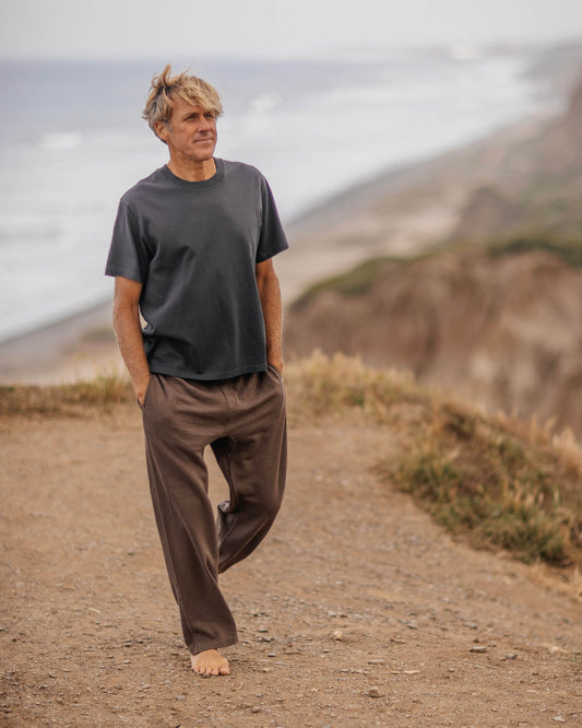 Man wearing brown sweats walking on a dirt path with mountains in the background