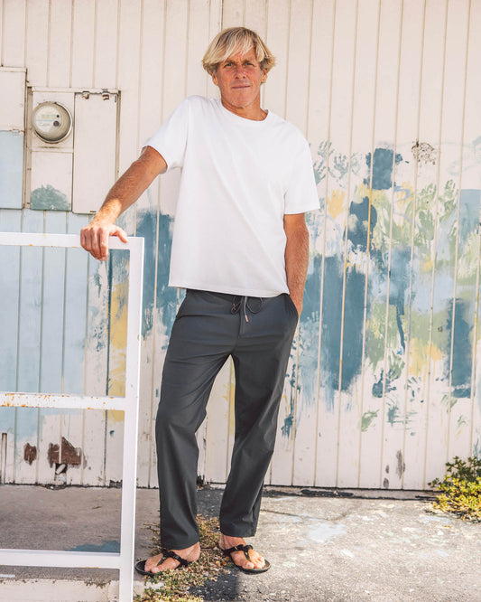 Person wearing a white t-shirt and dark pants standing against a colorful, weathered wall.