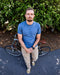Man in a blue shirt standing next to a bicycle with greenery in the background