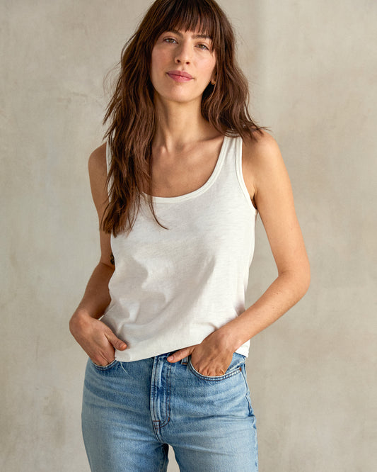 A woman wearing a white tank top and blue jeans.