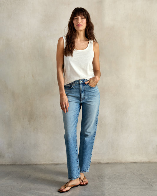 A woman wearing a white tank top and blue jeans.