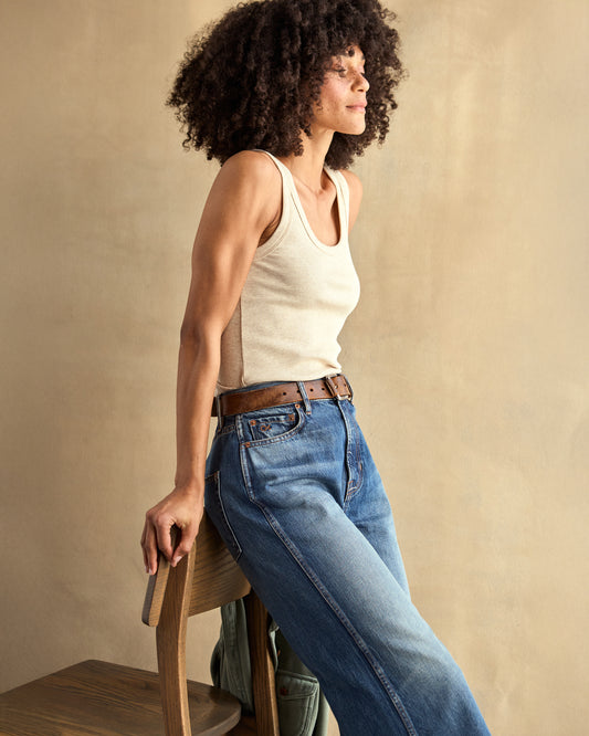 A woman wearing a beige ribbed tank top and blue jeans.