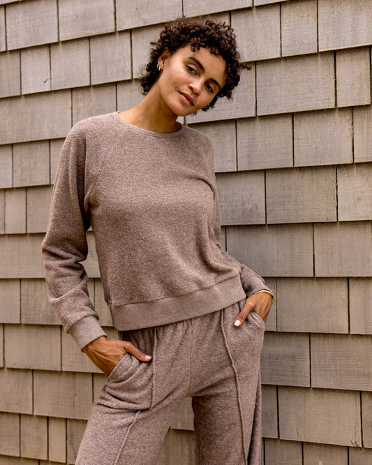 Woman wearing a beige sweater and pants against a wooden wall.