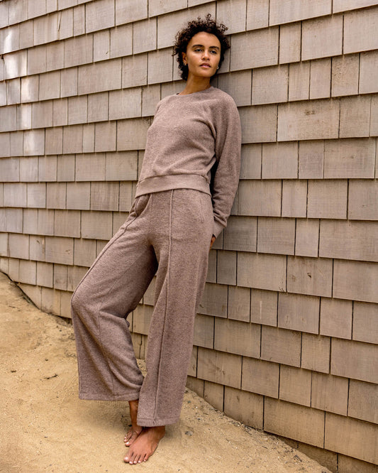 Woman in a beige outfit leaning against a wooden wall.