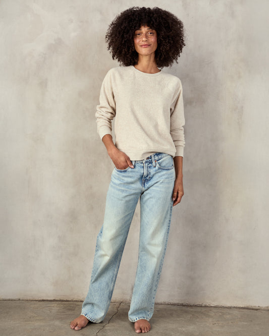 woman in cream sweatshirt and blue jeans  with a neutral background.