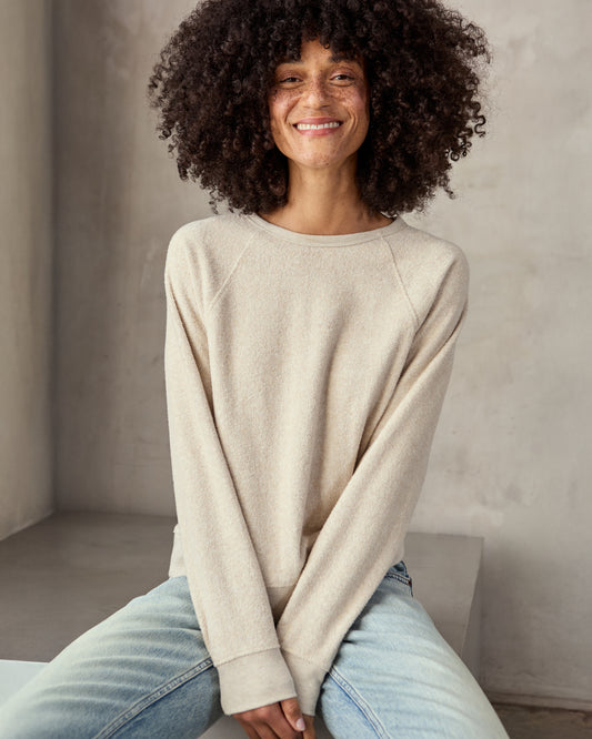 woman in cream sweatshirt and blue jeans  with a neutral background.