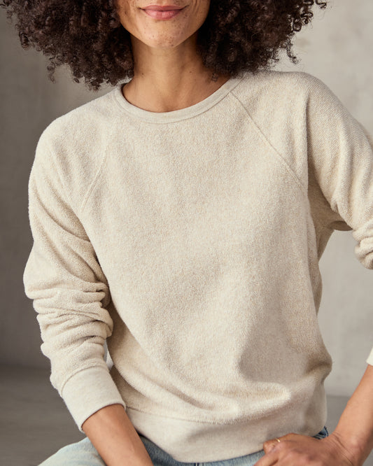 woman in cream sweatshirt and blue jeans  with a neutral background.