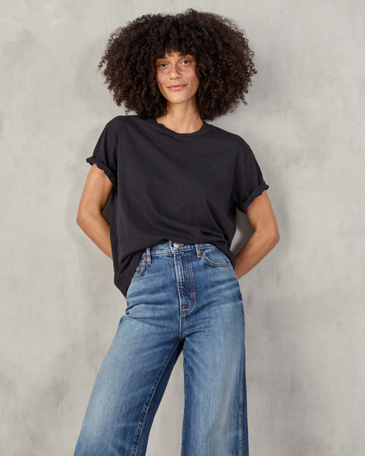 A woman sitting and wearing a black short-sleeved t-shirt and blue jeans.