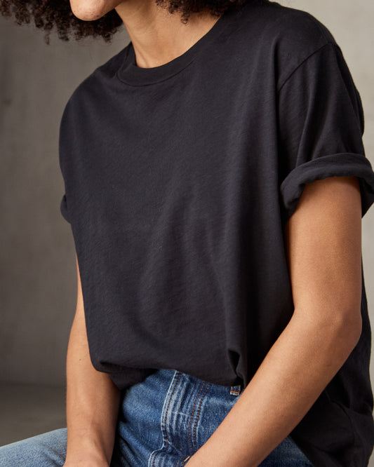 A woman sitting and wearing a black short-sleeved t-shirt and blue jeans.