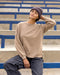 Person wearing a beige sweatshirt and brown beanie sitting on bleachers.