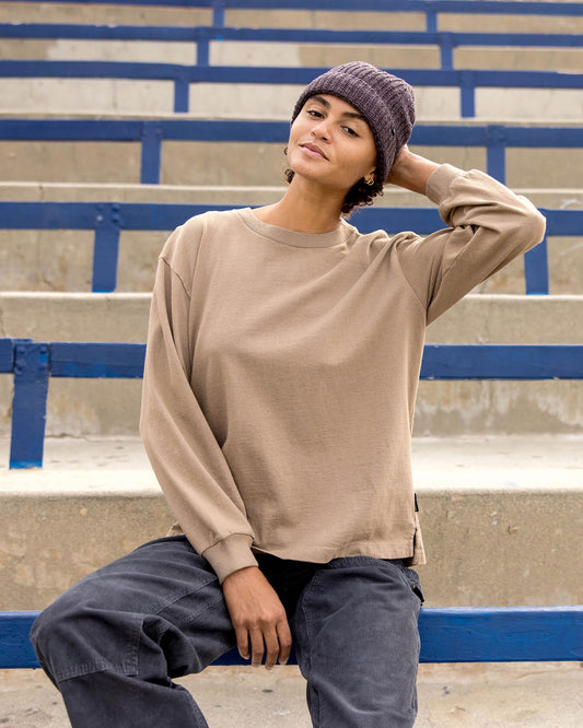 Person wearing a beige sweatshirt and brown beanie sitting on bleachers.
