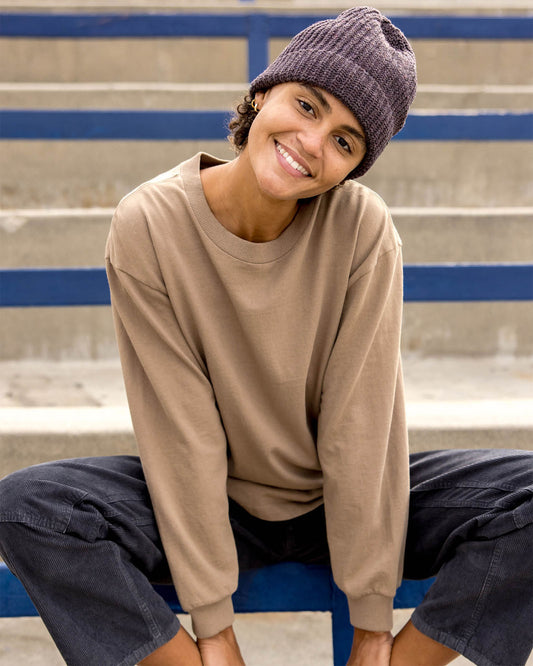 Person wearing a beige sweatshirt and brown beanie sitting on bleachers.