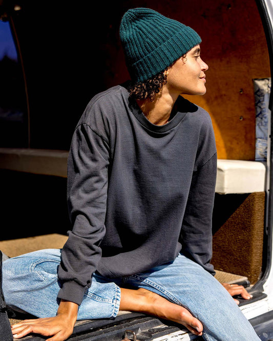 Person wearing a dark gray sweatshirt and teal beanie sitting inside a vehicle.