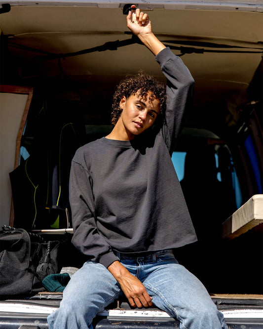 Person sitting inside a vehicle with an open roof, wearing a dark gray sweatshirt and blue jeans.