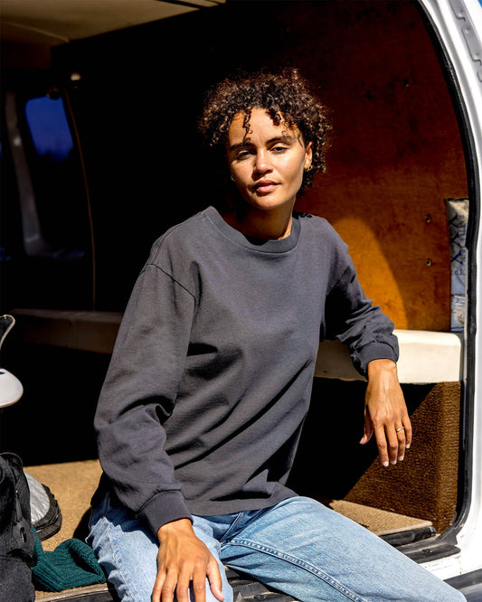 Person sitting inside a vehicle wearing a dark gray sweatshirt and blue jeans.