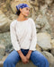 Woman sitting on rocks wearing a white sweater and blue jeans with a blue bandana.