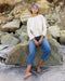 Person sitting on rocks wearing a white sweater and blue jeans with a headband.