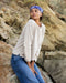 Woman wearing a white shirt and blue jeans with a headband, standing against a rocky background.