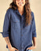 A woman wearing a long sleeve blue shirt with button-up front and chest pockets, paired with light blue denim shorts.