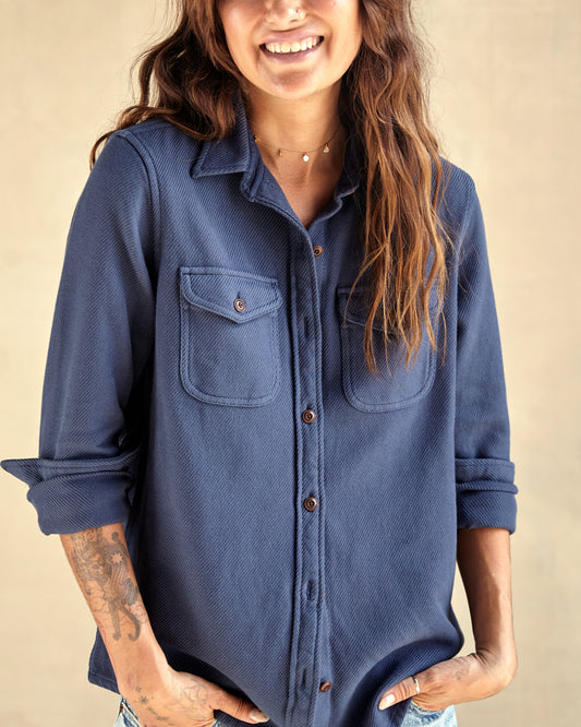 A woman wearing a long sleeve blue shirt with button-up front and chest pockets, paired with light blue denim shorts.