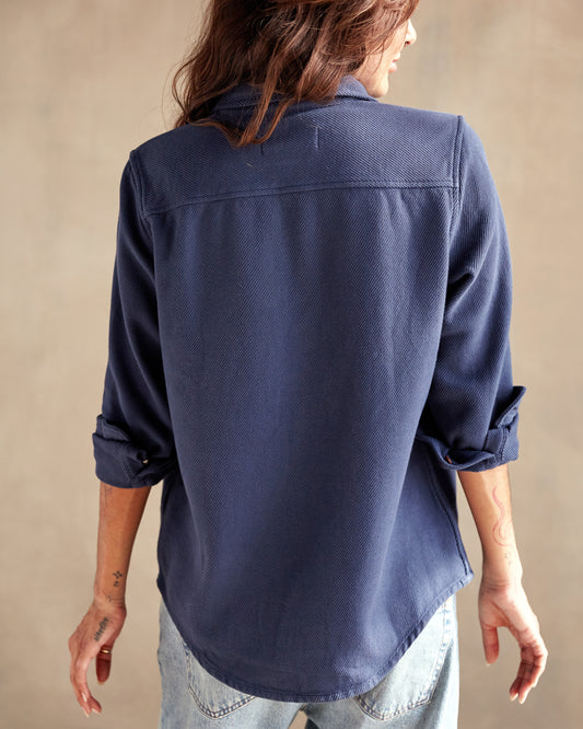 A woman wearing a long sleeve blue shirt with button-up front and chest pockets, paired with light blue denim shorts.