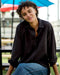 Person wearing a black shirt and blue jeans sitting outdoors under a blue umbrella.